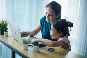 heureuse mère aidant sa jolie fille à étudier en ligne à la maison. parent et enfant regardant une leçon d'art ensemble sur un ordinateur portable photo