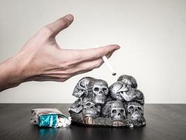 main masculine tenant la cigarette, crânes sur la table, concept anti-tabac photo