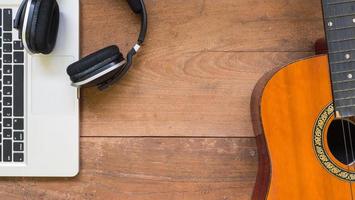 espace de travail vue de dessus avec ordinateur portable, casque et guitare acoustique sur fond de table en bois. photo