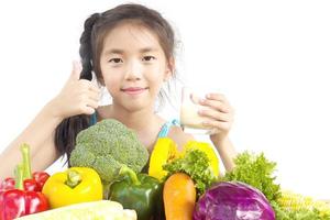 Jolie fille asiatique montrant profiter de l'expression avec des légumes frais colorés et un verre de lait isolé sur fond blanc photo