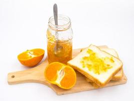 orange fraîche avec de la confiture d'orange dans un bocal en verre et du pain sur un plateau en bois sur fond blanc. photo