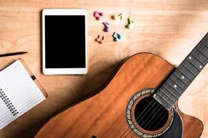 vue de dessus de guitare acoustique avec gadget d'ordinateur tactile tablette sur fond de table en bois. photo