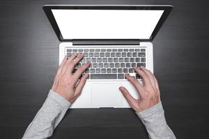 vue de dessus des mains mâles travaillant sur un ordinateur portable sur le fond du bureau en bois noir. photo