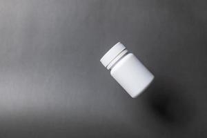 flacon de pilules en plastique blanc, sans étiquette, plafonné, flottant sur fond noir. photo