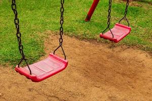 une balançoire rouge est attachée à deux vieilles chaînes rouillées dans la cour de récréation. dans le parc vu le sol et l'herbe photo