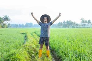 jeune agriculteur asiatique du millénaire debout et souriant avec se sent fier du succès de la culture du riz paddy dans la rizière. concept d'agriculture moderne. photo