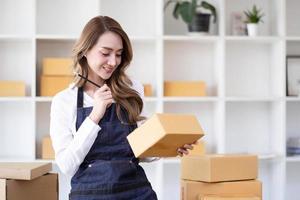 portrait d'une jeune femme asiatique sme travaillant avec une boîte à la maison le lieu de travail. propriétaire de petite entreprise de démarrage, entrepreneur de petite entreprise sme ou entreprise indépendante en ligne et concept de livraison. photo