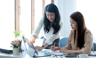 deux jeunes femmes d'affaires asiatiques discutent de la stratégie de travail et de planification du projet d'investissement. gens d'affaires parlant avec un ordinateur portable au bureau. photo