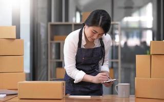 portrait, entrepreneur, jeune femme asiatique, entreprise indépendante, PME, achats en ligne, travail sur ordinateur portable avec boîte à colis sur la table du bureau à domicile, commerce en ligne et concept de livraison. photo