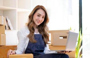 portrait d'une jeune femme asiatique sme travaillant avec une boîte à la maison le lieu de travail. propriétaire de petite entreprise de démarrage, entrepreneur de petite entreprise sme ou entreprise indépendante en ligne et concept de livraison. photo