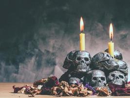 crânes avec bougie allumée et fleurs séchées sur fond sombre. photo