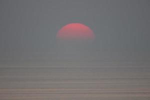 le soleil tombe dans la mer et est partiellement avalé par le brouillard. le ciel est sombre photo