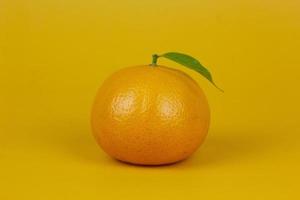 un fruit orange avec une feuille verte isolée sur fond jaune. un fruit orange avec support de feuilles sur le concept d'isolement pour la conception d'annonces photo