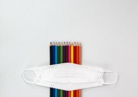 ensemble de crayons colorés, masque facial isolé sur fond blanc. concept de retour à l'école pour l'ouverture d'un nouveau trimestre. sur la conception du modèle de vue de dessus photo