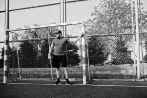 jeune homme musclé barbu brutal portant une chemise rouge, un short et une casquette au stade. photo