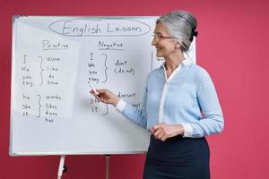 femme âgée enseignant la langue anglaise tout en se tenant près du tableau blanc sur fond rose photo
