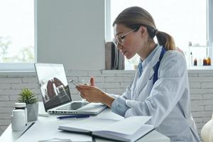 femme médecin confiante utilisant un téléphone intelligent tout en étant assise au cabinet médical photo