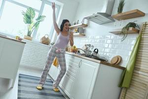 toute la longueur d'une jeune femme utilisant un fouet comme microphone pendant la cuisson à la cuisine photo