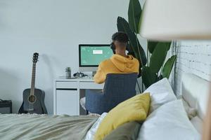 vue arrière d'un homme africain utilisant un ordinateur assis sur son lieu de travail à la maison photo