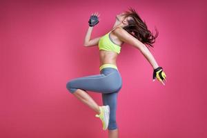 jeune femme confiante en vêtements de sport faisant de l'exercice sur fond rose photo