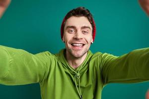 heureux jeune homme regardant à travers un cadre de doigt en se tenant debout sur fond vert photo