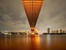 oreng a mené la lumière sous le pont au-dessus de la rivière un jour nuageux dans le ciel. pont bhumibol, samut prakan, thaïlande photo