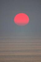 le soleil tombe dans la mer et est partiellement avalé par le brouillard. le ciel est sombre photo