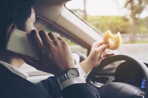 un homme se précipite au volant d'une voiture à l'aide d'un téléphone portable et mange dangereusement de la restauration rapide photo