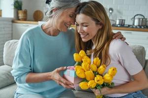 femme âgée heureuse et sa fille adulte assise sur le canapé et tenant un bouquet de tulipes photo