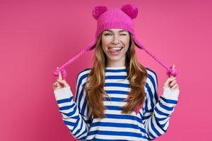 jeune femme espiègle ajustant son chapeau rose en se tenant debout sur un fond coloré photo