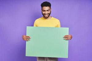 bel homme africain tenant une bannière verte et souriant en se tenant debout sur fond violet photo