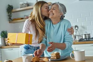 jeune femme embrassant sa mère et tenant une boîte-cadeau tout en passant du temps à la cuisine ensemble photo