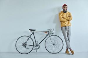 heureux jeune homme africain appuyé contre le mur tout en se tenant près de son vélo photo