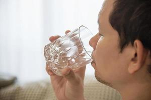 un homme asiatique boit de l'eau après s'être réveillé le matin assis sur un lit - concept de soins de santé photo