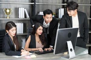 équipe multiage d'affaires réussie debout autour de l'ordinateur pour la présentation du travail. groupe de gens d'affaires lors d'une réunion au bureau, travaillant sur ordinateur photo