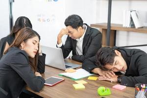 membres de l'équipe commerciale dormant sur un bureau et des chaises. une équipe commerciale est fatiguée d'une longue réunion. photo