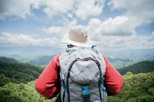 jeune homme en randonnée sur le rocher supérieur, sac à dos homme regardant la belle vallée de montagne à la lumière du soleil en été, paysage avec homme sportif, hautes collines, forêt, ciel. voyage et tourisme. photo