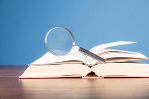 livre ouvert avec loupe sur un bureau en bois dans la bibliothèque d'informations de l'école ou de l'université, concept pour l'éducation, la lecture, l'étude, l'espace de copie et le fond bleu. photo