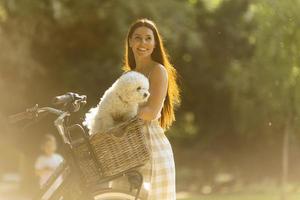 jeune femme avec chien bichon blanc frisé dans le panier de vélo électrique photo