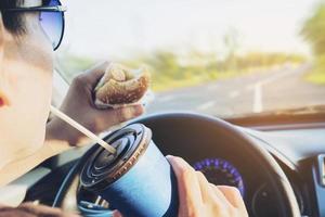 l'homme mange dangereusement des hot-dogs et des boissons froides en conduisant une voiture photo