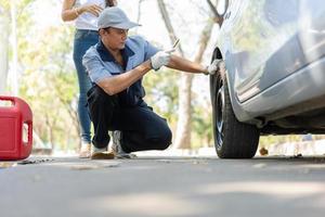 expertise mécanicien homme en uniforme utilisant la force essayant de dévisser les écrous de boulons de roue et aider une femme à changer de roue de voiture sur l'autoroute, service de voiture, réparation, concept d'entretien. photo