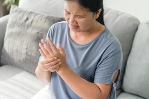 gros plan femme assise sur un canapé tient son poignet. blessure à la main, sensation de douleur. soins de santé et concept médical. photo