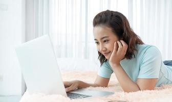 jeune femme de beauté asiatique travaillant sur un ordinateur portable dans le lit à la maison