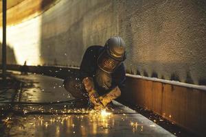 Étincelle de coupe de métal travailleur masculin sur la plaque d'acier du fond du réservoir avec flash de lumière de coupe gros plan porter des gants et un masque de protection