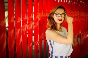 jolie femme rousse à lunettes posant sur fond rouge. photo