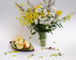 nature morte de fleurs sauvages et d'une pomme sur une soucoupe, le tout sur un fond clair photo