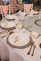 composition florale pour mariage d'été, faite de roses et de branches vertes sur une table de dîner au restaurant. , verre et assiettes dans le restaurant à l'extérieur par une journée venteuse avec effet de grain de film photo