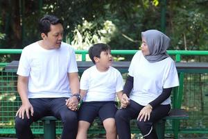 jeune famille asiatique assise ensemble et ayant une conversation au parc de verdure. bien-être et bien-être familial. photo