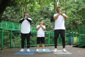 jeune mère et père asiatique pratiquant le yoga et s'étirant avec son fils dans le parc verdoyant. photo