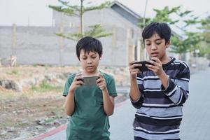 deux enfants avec des gadgets. frères surfant sur le net ou jouant à des jeux en ligne sur smartphone et tablette numérique à l'extérieur en se tenant debout. concept moderne de communication et de dépendance aux gadgets. photo